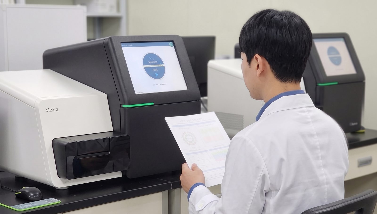 연구원이 MiSeq 시퀀서 앞에서 마이크로바이옴 분석 결과지를 확인하는 모습